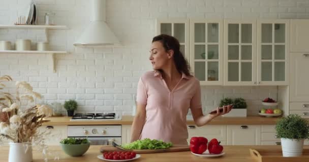 Happy carefree housewife listen music dancing while cooking in kitchen - Séquence, vidéo