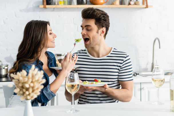 happy woman holding plate and feeding boyfriend with lettuce  - Foto, Imagem