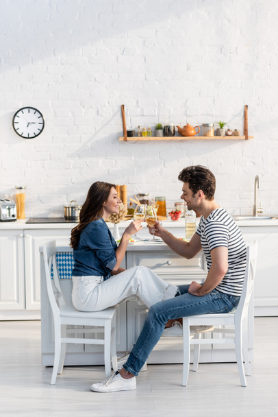 side view of happy couple clinking glasses with wine in kitchen  - Photo, Image