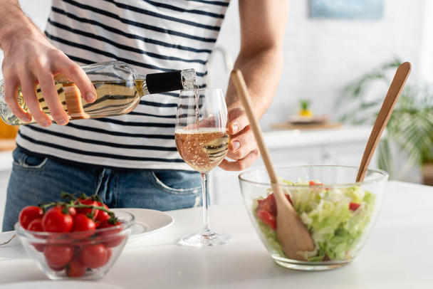 cropped view of man pouring white wine in glass near salad  - Foto, afbeelding