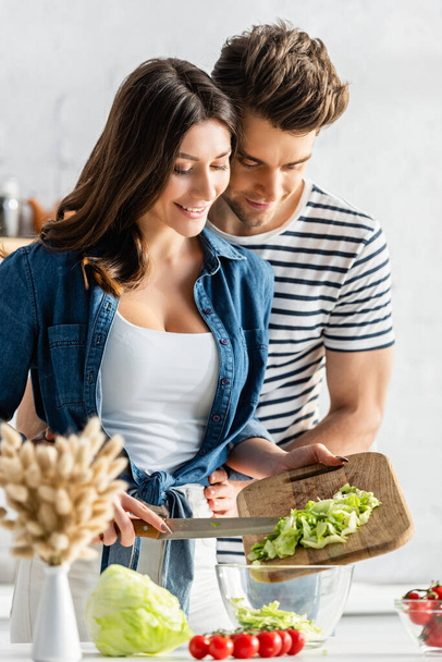 cheerful couple preparing salad in kitchen with catkins on blurred foreground - Foto, imagen