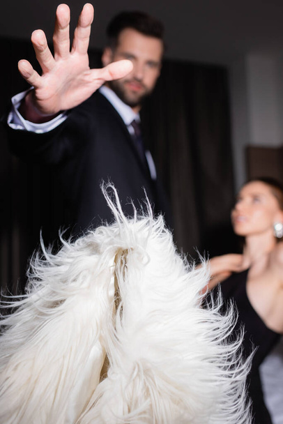 Man in suit throwing fluffy jacket near girlfriend on blurred background in hotel  - Photo, Image