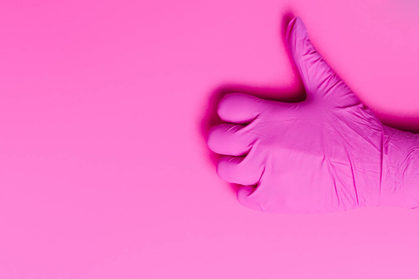 Como sobre un fondo rosa. Una mano en un guante de color rosa látex muestra el pulgar hacia arriba. Espacio lateral vacío. - Foto, Imagen