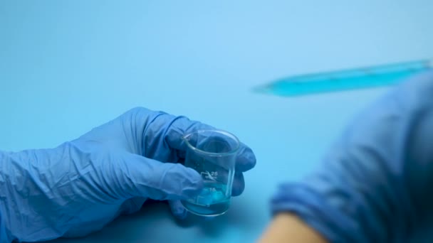 Mavi arka planı olan modern bir laboratuvarda, birinden diğerine mavi tıbbi sıvıyı döken iki cam şişenin sanatsal yakın çekimi. Araştırma ve geliştirme kavramı. - Video, Çekim