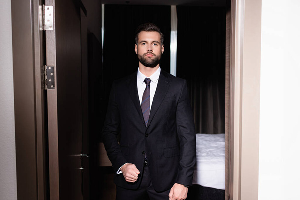 Bearded man in formal wear looking at camera in hotel room during night - 写真・画像