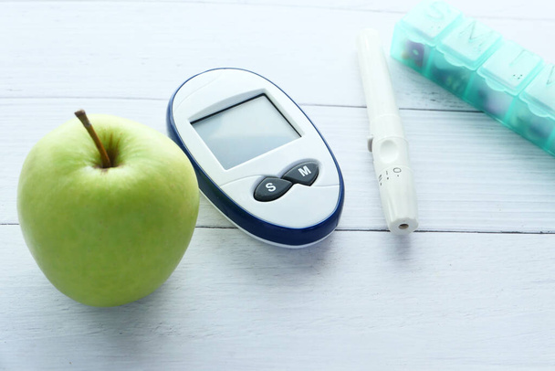 Κοντινό πλάνο των διαβητικών εργαλείων μέτρησης, μήλο και κουτί χάπι στο τραπέζι  - Φωτογραφία, εικόνα
