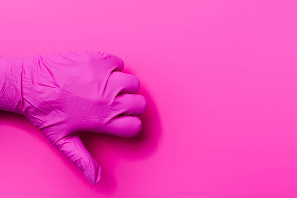 Una mano de un paramédico en un guante rosa muestra una aversión sobre un fondo rosa con espacio lateral. Pulgar hacia abajo. - Foto, Imagen