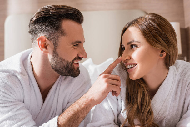 Lächelnder Mann im Bademantel berührt Nase von Freundin im Hotel  - Foto, Bild