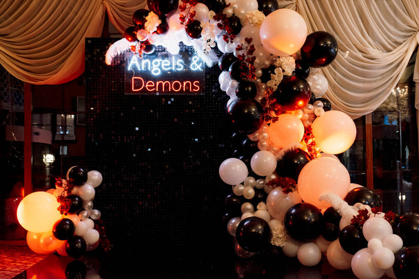 una zona de fotos temática ángeles y demonios en negro con bolas y plumas blancas y negras - Foto, imagen