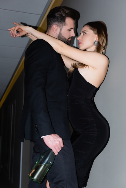 Sexy woman hugging boyfriend with bottle of champagne in hotel during night  - Φωτογραφία, εικόνα