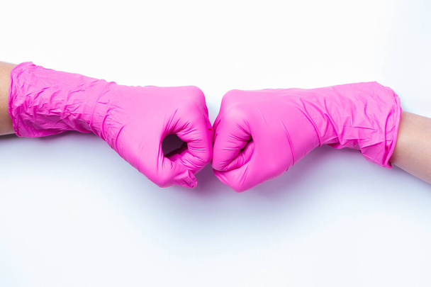 Las manos en guantes de látex rosa saludan puño en puño. Nuevo concepto de saludo durante una pandemia y sobre un fondo blanco. - Foto, Imagen
