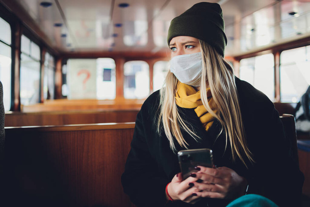 Ένα κορίτσι με προστατευτική μάσκα σε ένα βαγόνι του μετρό με ένα κινητό τηλέφωνο στα χέρια της. - Φωτογραφία, εικόνα