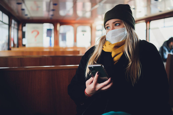 Una chica con una máscara protectora en un vagón subterráneo con un teléfono móvil en sus manos. - Foto, Imagen