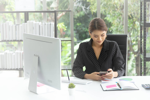 Młoda uśmiechnięta kobieta biznesu siedzi przy stole za pomocą smartfona handlu online, sprawdzając giełdę i e-mail. Student uczenia się online. - Zdjęcie, obraz
