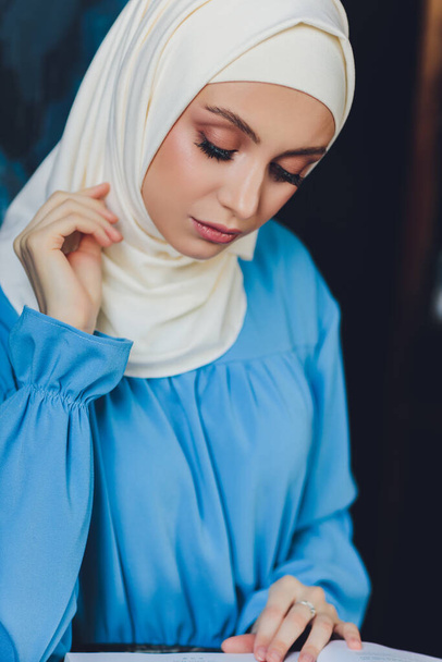 Portrait of a beautiful Asian muslim woman model wearing white blouse and blue hijab posing on white curtain as background in close-up view. - Foto, afbeelding