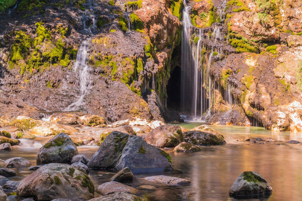 Waterval omringd door rotsen en wilde planten - Foto, afbeelding