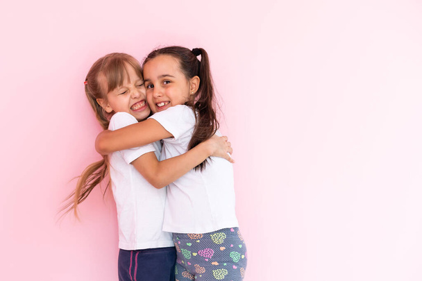 Two little girls hugging each other. Isolated on on a pink background - Photo, Image