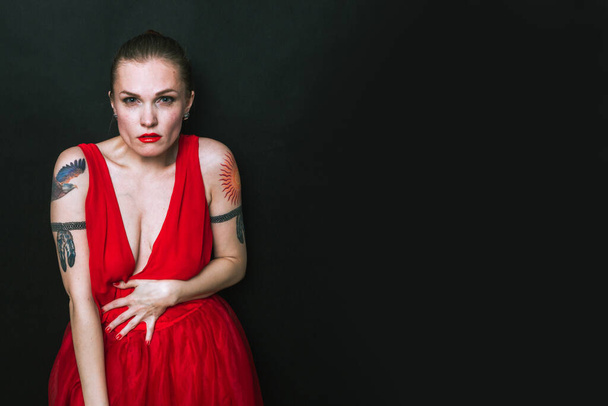 Μόδα μοντέλο σε κόκκινο φόρεμα ομορφιάς. Σέξι γυναίκα με τατουάζ ποζάρει με βραδινό φόρεμα. Φωτογραφία στούντιο με μαύρο απομονωμένο φόντο - Φωτογραφία, εικόνα