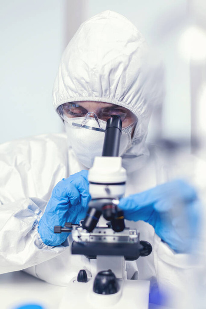 Ιατρικός μηχανικός σε κοστούμι PPE στο σύγχρονο εργαστήριο κοιτάζοντας το δείγμα - Φωτογραφία, εικόνα