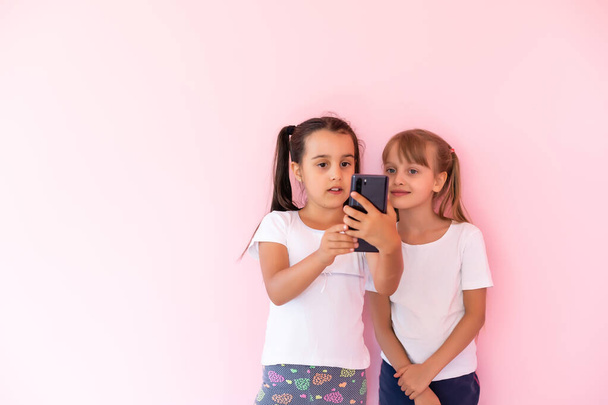 Dvě holčičky hrající si s chytrými telefony na růžovém pozadí - Fotografie, Obrázek