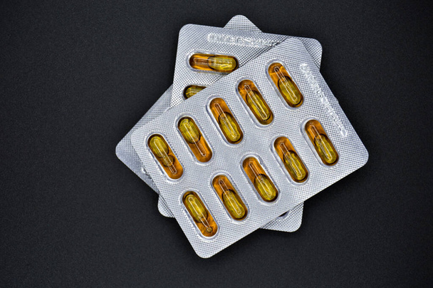 Comprimidos de comprimidos ovais de óleo de peixe amarelo embalados, isolados em fundo preto, comprimidos ovais médicos - Foto, Imagem