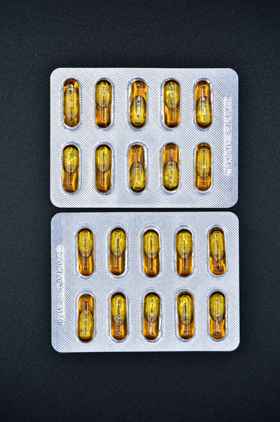 Tabletki owalne żółte olej rybny pakowane, izolowane na czarnym tle, tabletki owalne medyczne - Zdjęcie, obraz