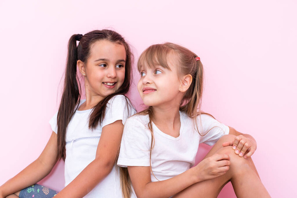 two little girl sitting on floor and looking up. Isolated on a pink background - Foto, Imagem