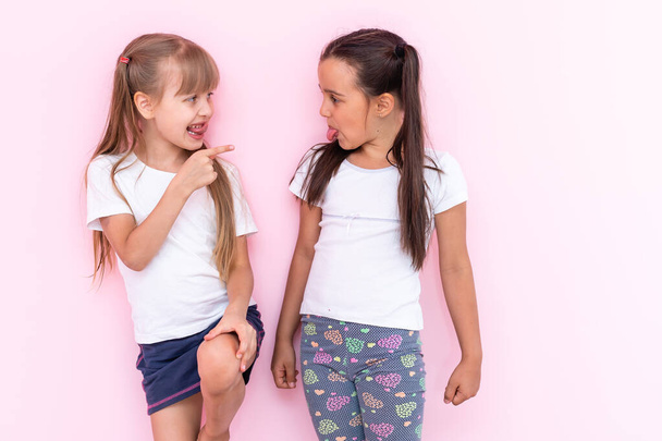 Obrázek dvou rozzlobených dospívajících dívek s copánky v ležérním oblečení stojící zády k sobě s rukama zkříženýma na růžovém pozadí - Fotografie, Obrázek