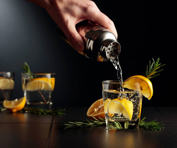 Cocktail Gin en Tonic met citroen en rozemarijn. De barman schenkt een cocktail van een shaker in een glas. - Foto, afbeelding