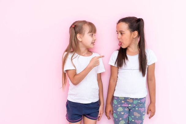 Immagine di due ragazze adolescenti arrabbiate con trecce in abiti casual in piedi isolate su sfondo rosa - Foto, immagini