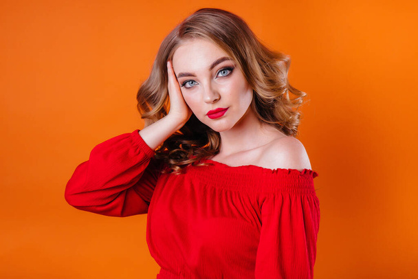 A young beautiful girl shows emotions and smiles in the Studio on an orange background. Girls for advertising - Фото, зображення