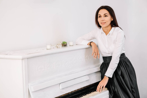 Beautiful woman dressed in white shirt playing on white piano. Place for text or advertising. - Valokuva, kuva