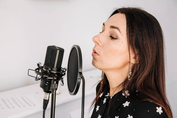 Portrait of beautiful woman sings a song near a microphone in a recording studio. Place for text or advertising. - Photo, Image