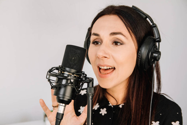 Portrait of beautiful woman in headphones sings a song near a microphone in a recording studio.. Place for text or advertising. - Photo, Image