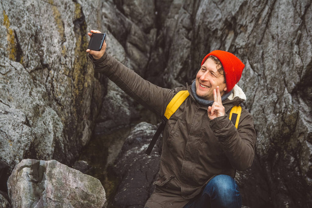 Hombre viajero tomando autorretrato con un teléfono inteligente sobre el fondo de montañas y rocas. Lugar para texto o publicidad. - Foto, Imagen