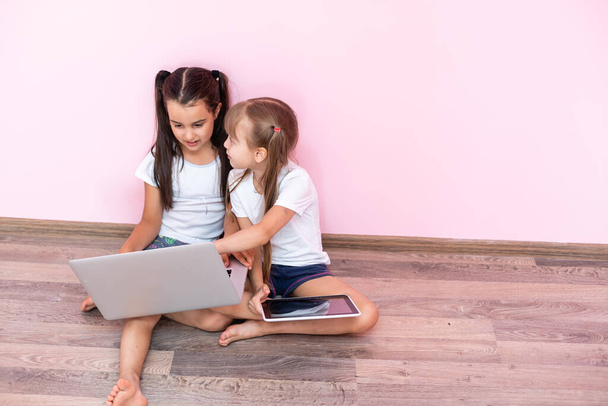 Zwei kleine Mädchen sitzen vor einem Laptop und lachen, Nahaufnahme, positive Emotionen, Unterhaltung im Internet für Kinder - Foto, Bild