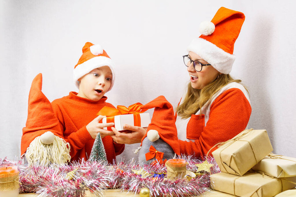 Ein Junge und ein Mädchen im roten Zwergenkostüm betrachten die Schachtel mit einem Weihnachtsgeschenk. Skandinavische Gnomen. Weihnachtsferien-Konzept - Foto, Bild