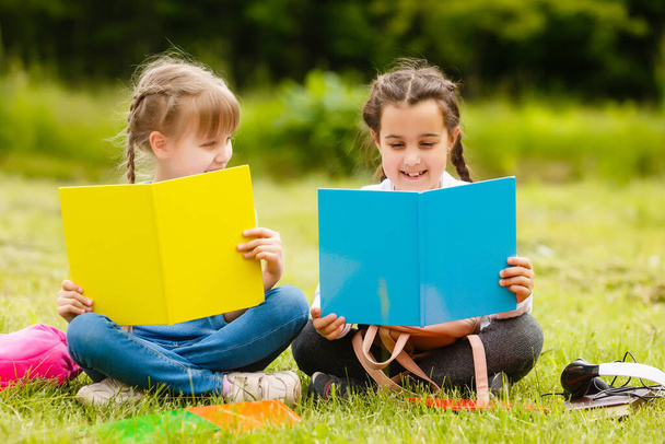 Kaksi kaunista koulutyttöä istuu kirjojen kanssa ulkona puistossa. Koulutyttöjä tai opiskelijoita opetetaan luonnossa. - Valokuva, kuva