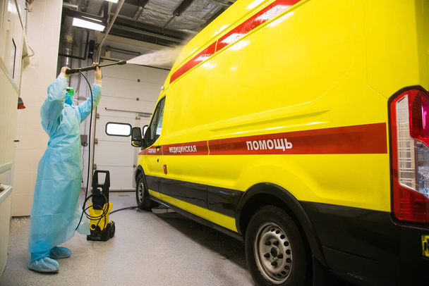 Desinfectie van de ambulance. Een paramedicus behandelt een ambulance met een desinfecterende oplossing met een spuitpistool om de verspreiding van het coronavirus te voorkomen (Covid-19). Inschrijving op de auto: reanimatie. Spoedeisende medische zorg - Foto, afbeelding