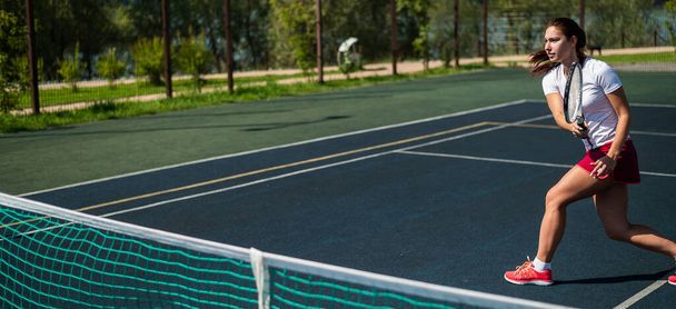 Sportive caucasian woman playing tennis on an outdoor court. Widescreen. - 写真・画像