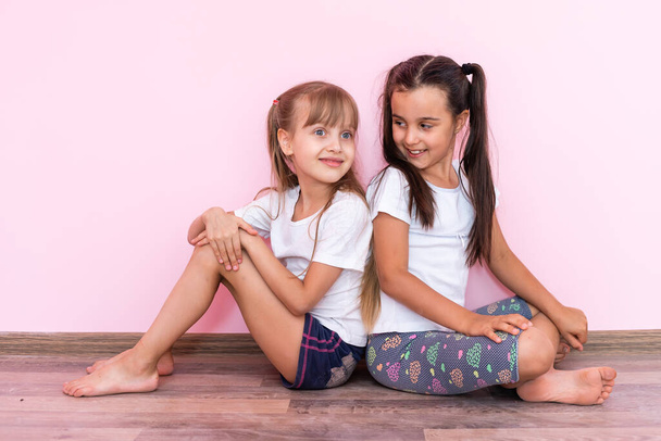 A child, two girls sitting on the floor. Isolated on pink background - Photo, Image