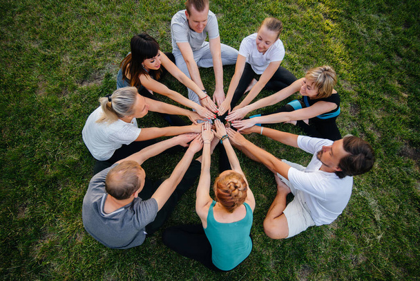 Un gruppo di persone fa yoga in cerchio all'aria aperta durante il tramonto. Stile di vita sano, meditazione e benessere - Foto, immagini