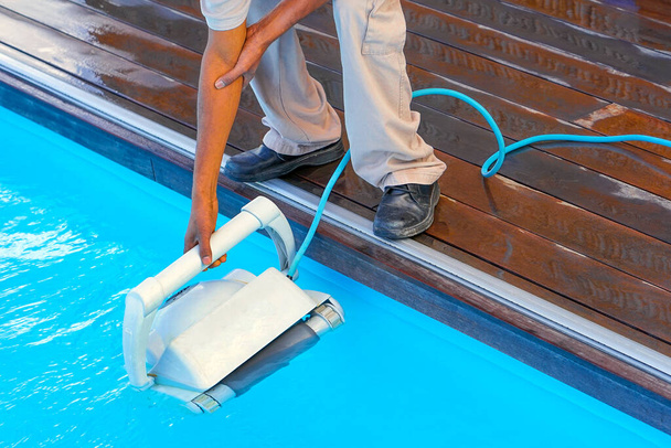 A pool cleaner holds a robot cleaner. Pool cleaner during his work. African hotel staff worker cleaning the pool. - Photo, Image