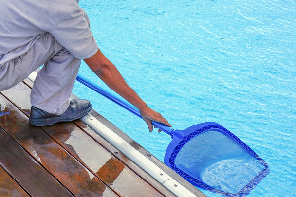 Um limpador de piscinas tem um robô limpo. Limpeza de piscinas durante o trabalho. Trabalhador africano da equipe do hotel limpando a piscina. - Foto, Imagem