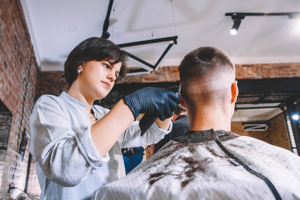Красива жінка-перукар робить зачіску на голову клієнта з електричним тримером в перукарні. Концепція рекламного та перукарського магазину. Місце для тексту або реклами
. - Фото, зображення