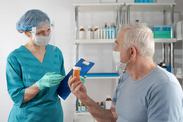 Female nurse holding a clipboard folder, giving prescription drug orange pill jar  to adult senior man. Doctor's appointment hospital healthcare case - Foto, Imagem