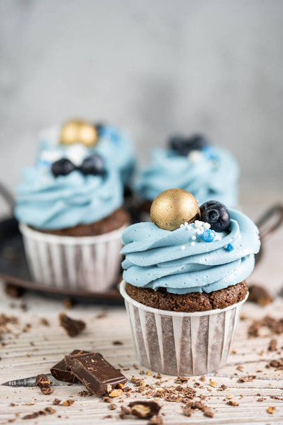 Several muffins or cupcakes with blue shaped cream and blueberrieson at white table. Rustic style copyspace. - Foto, Bild