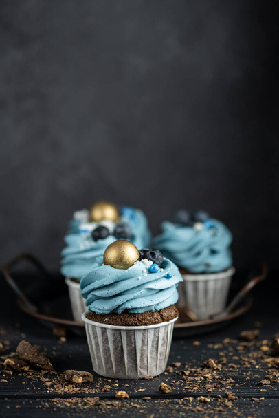 Several muffins or cupcakes with blue shaped cream and blueberrieson at black table. Rustic style copyspace. - Fotó, kép