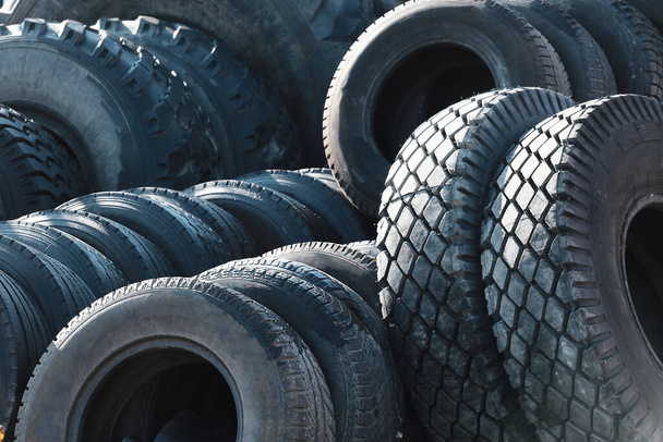 Reciclaje de neumáticos para camiones. Eso es un montón de neumáticos calvos negros de goma que yacen afuera en un almacén abierto. - Foto, Imagen