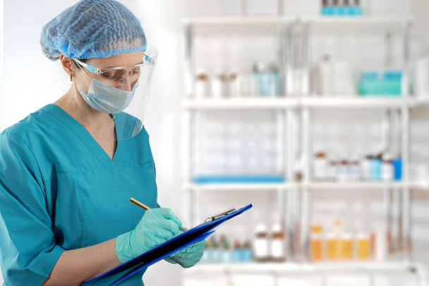 Päivystävä naispuolinen ensihoitaja kirjoittaa tietoja siniseen pidikkeeseen hämärtyneeseen taustaan hyllyillä ja lääkkeillä - Valokuva, kuva